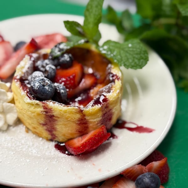 A Capp's Pizzeria dessert with berries, powdered sugar, and mint on a white plate.