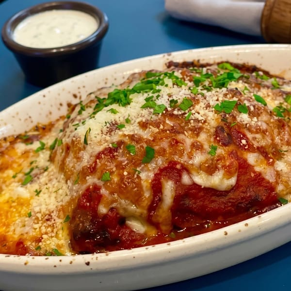 Baked lasagna with melted cheese, red sauce, and parsley in a white dish, with a side of ranch.