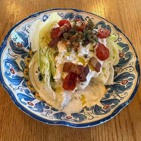 A wedge salad with cherry tomatoes, bacon, and dressing on a decorative blue and white plate.
