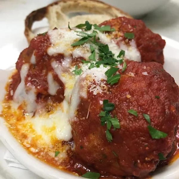 Three meatballs covered in red sauce, melted cheese, and fresh parsley, with a slice of bread.