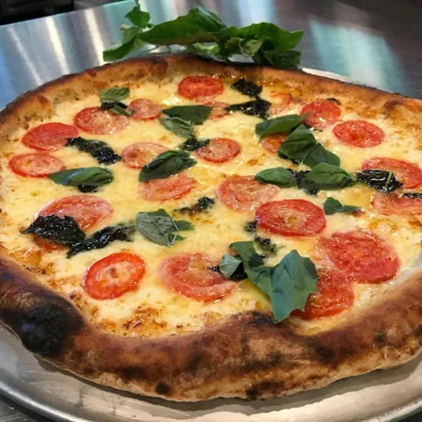 A Capp's Pizzeria & Trattoria pizza with melted cheese, sliced tomatoes, and fresh basil.