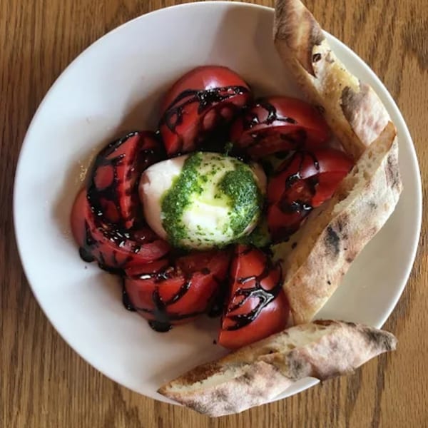 Capp's Pizzeria & Trattoria's Caprese salad with sliced tomatoes, mozzarella, pesto, balsamic glaze, and bread.