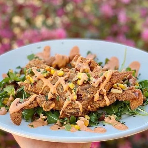 Crispy fried soft-shell crab drizzled with sauce, served on a bed of arugula and corn.